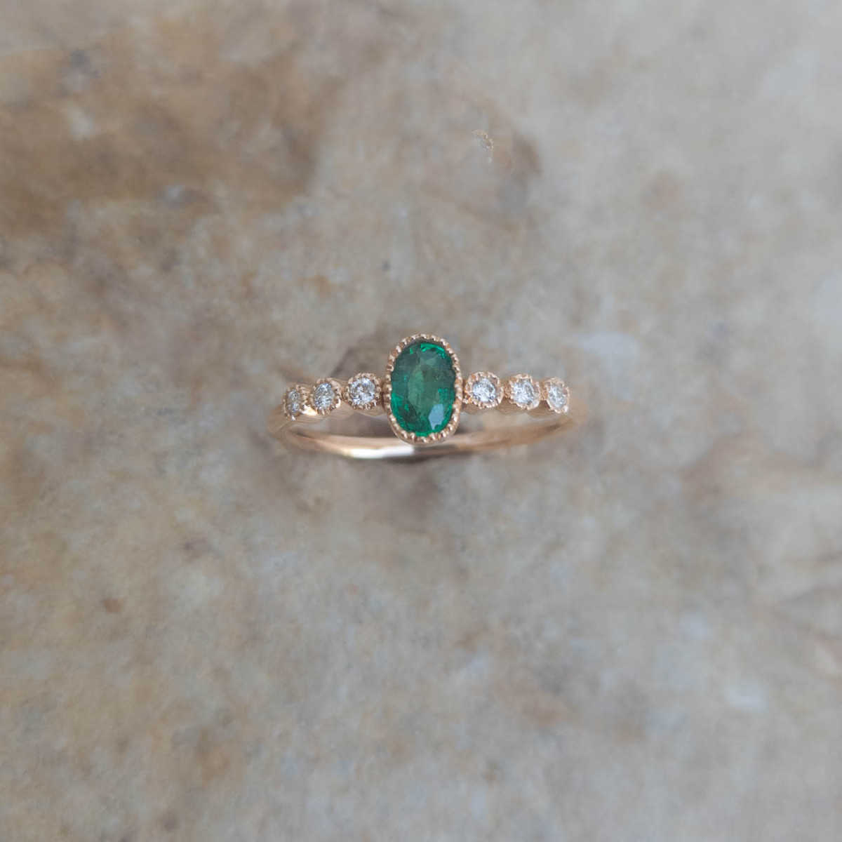 Une bague en or rose 18k sertie au centre d'une émeraude et sur les côtés de diamants Une bague en or rose 18k sertie au centre d'une émeraude et sur les côtés de diamants